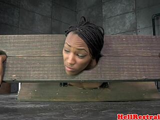 Bound ebony sub in pillory contrasts with intense spanking session from dominant partner